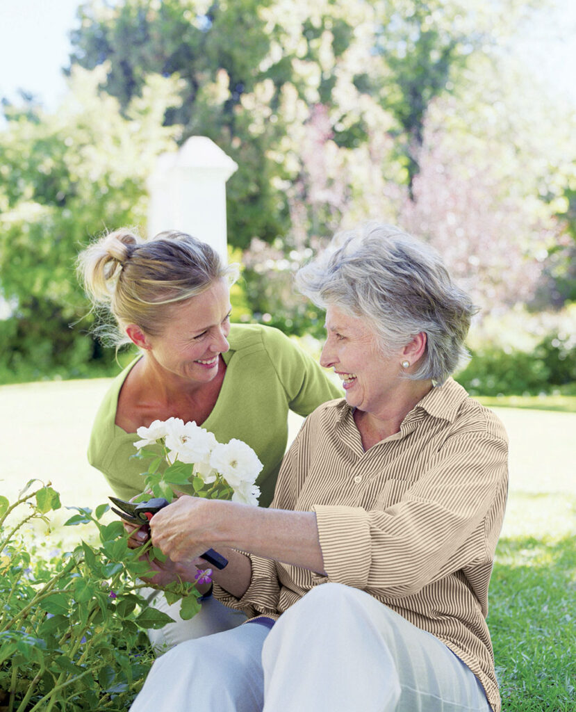 A caregiver in the backyard, gently attending to a senior seated on the grass, offering support with care and attention.